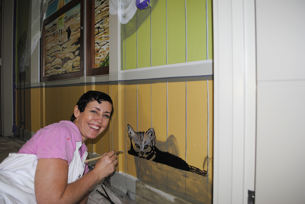 artist sharron tancred hand-painting a mural for dementia across an exit door